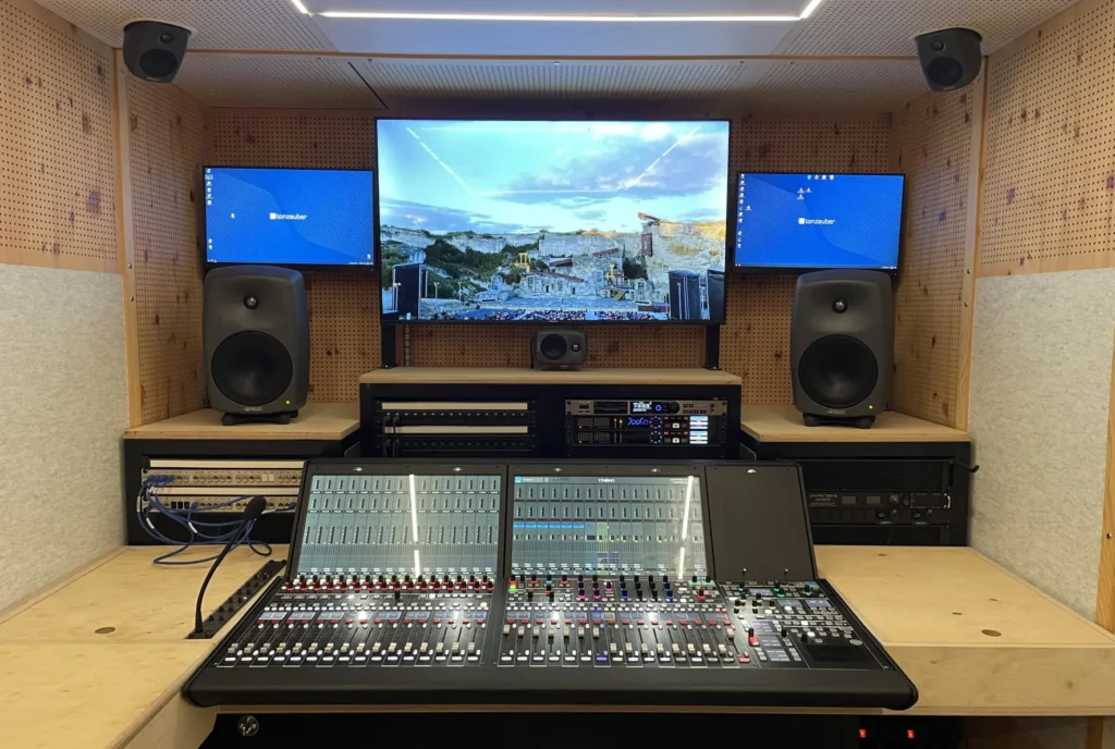 An audio production suite with a mixing console, speakers, and three monitors on the desk.